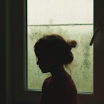 Girl Standing near Window with Raindrops