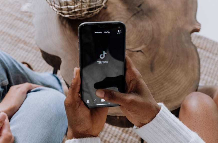 Close-up of hands holding a smartphone displaying the TikTok app interface on a wooden surface.