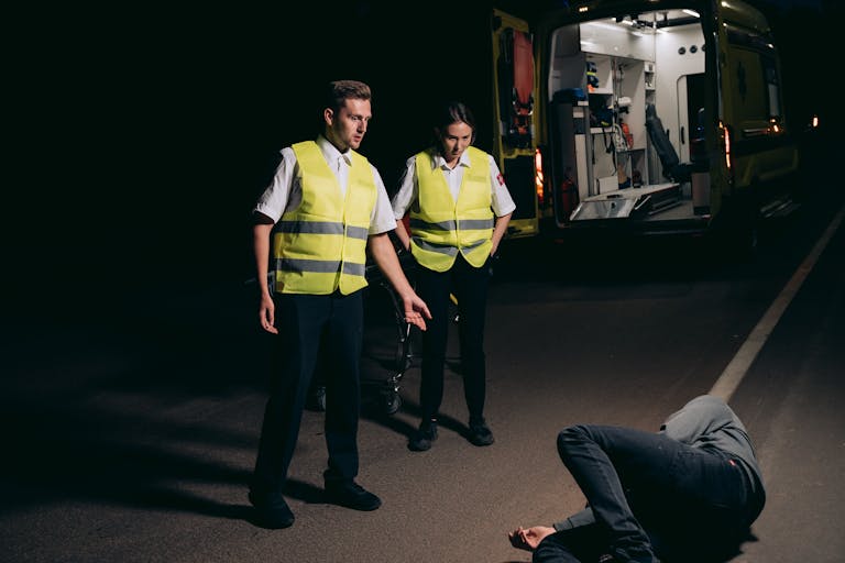 Paramedics assist a patient on a dimly lit street, showcasing emergency response at night.