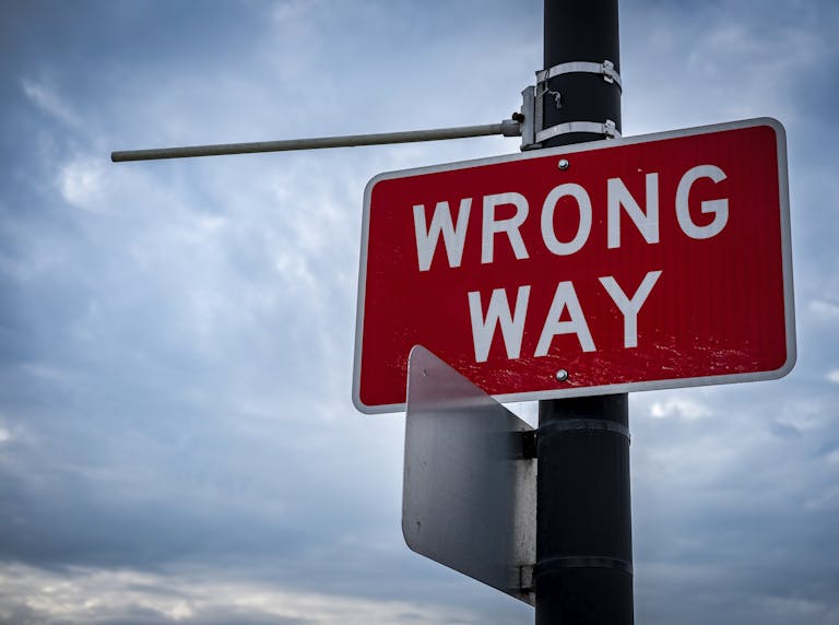 A close-up of a red wrong way road sign against an overcast sky, symbolizing caution.
