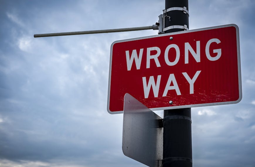 A close-up of a red wrong way road sign against an overcast sky, symbolizing caution.