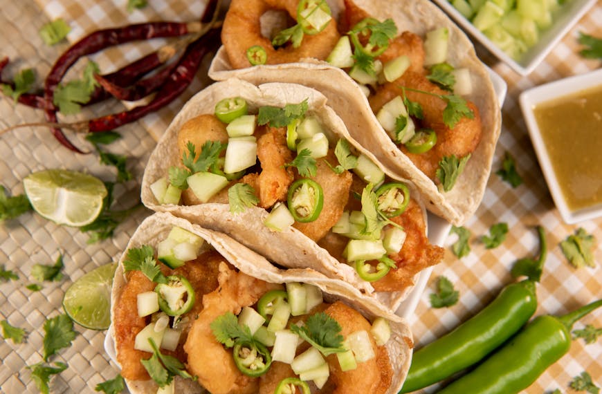 Three appetizing Mexican street tacos topped with fresh jalapeños, lime, and cilantro, served on a checkered tablecloth.