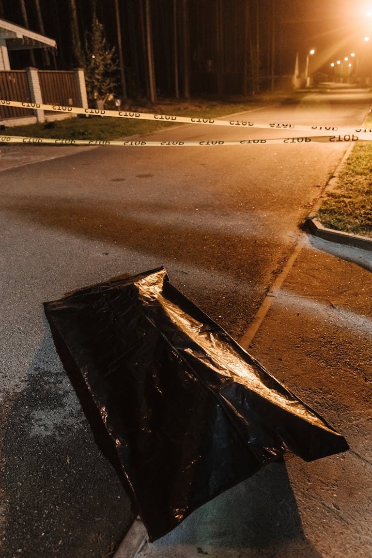 Urban crime scene with police tape and evidence bag under streetlights at night.