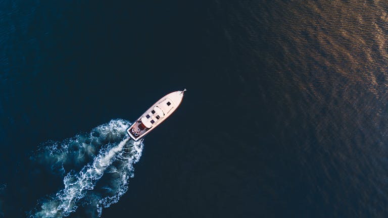 Aerial view of a luxury yacht cruising through the ocean waters with a trail of white waves behind.