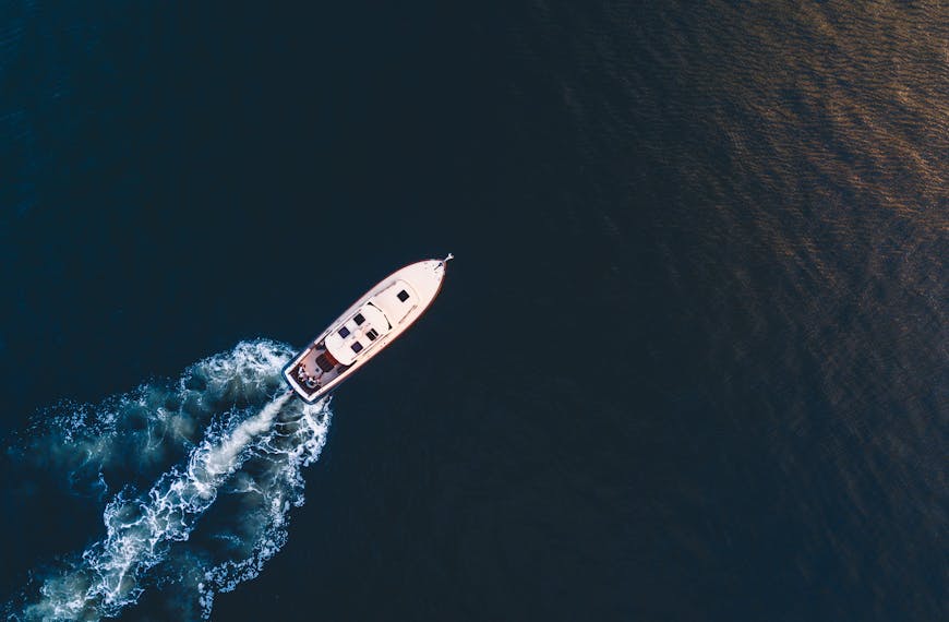 Aerial view of a luxury yacht cruising through the ocean waters with a trail of white waves behind.