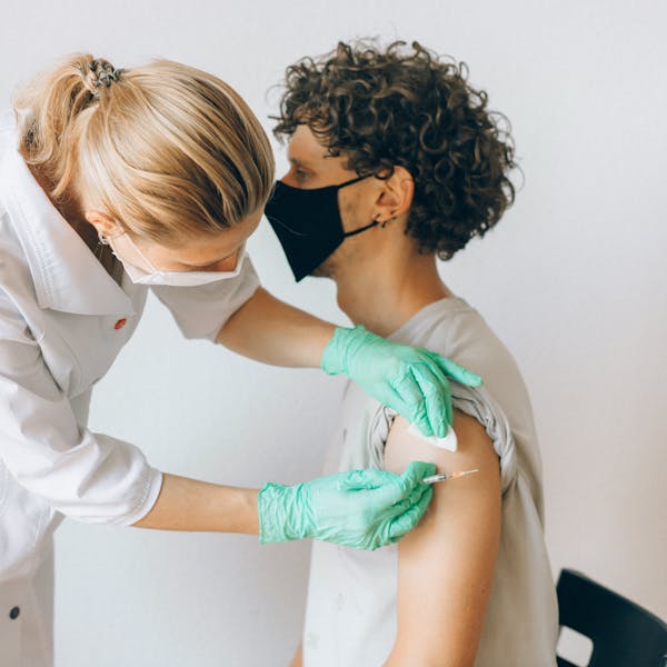 A healthcare worker gives a vaccine shot to a patient wearing a mask, highlighting medical safety and health precautions.