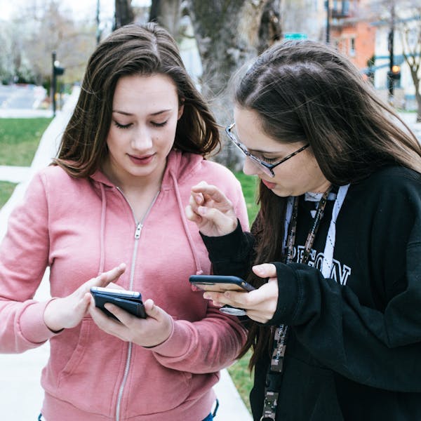 Two young women using smartphones outdoors, sharing information.
