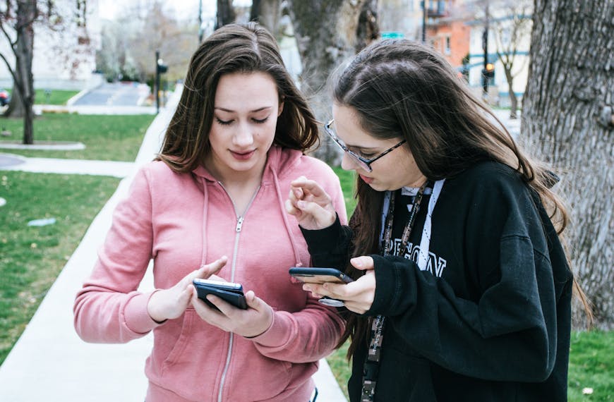 Two young women using smartphones outdoors, sharing information.