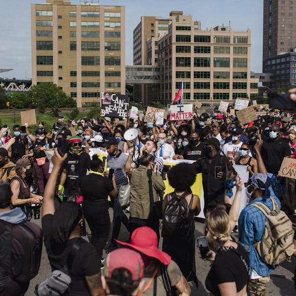 A large and diverse crowd gathers for a peaceful protest advocating for racial justice and equality in an urban setting.