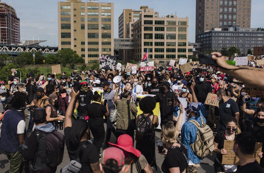 A large and diverse crowd gathers for a peaceful protest advocating for racial justice and equality in an urban setting.