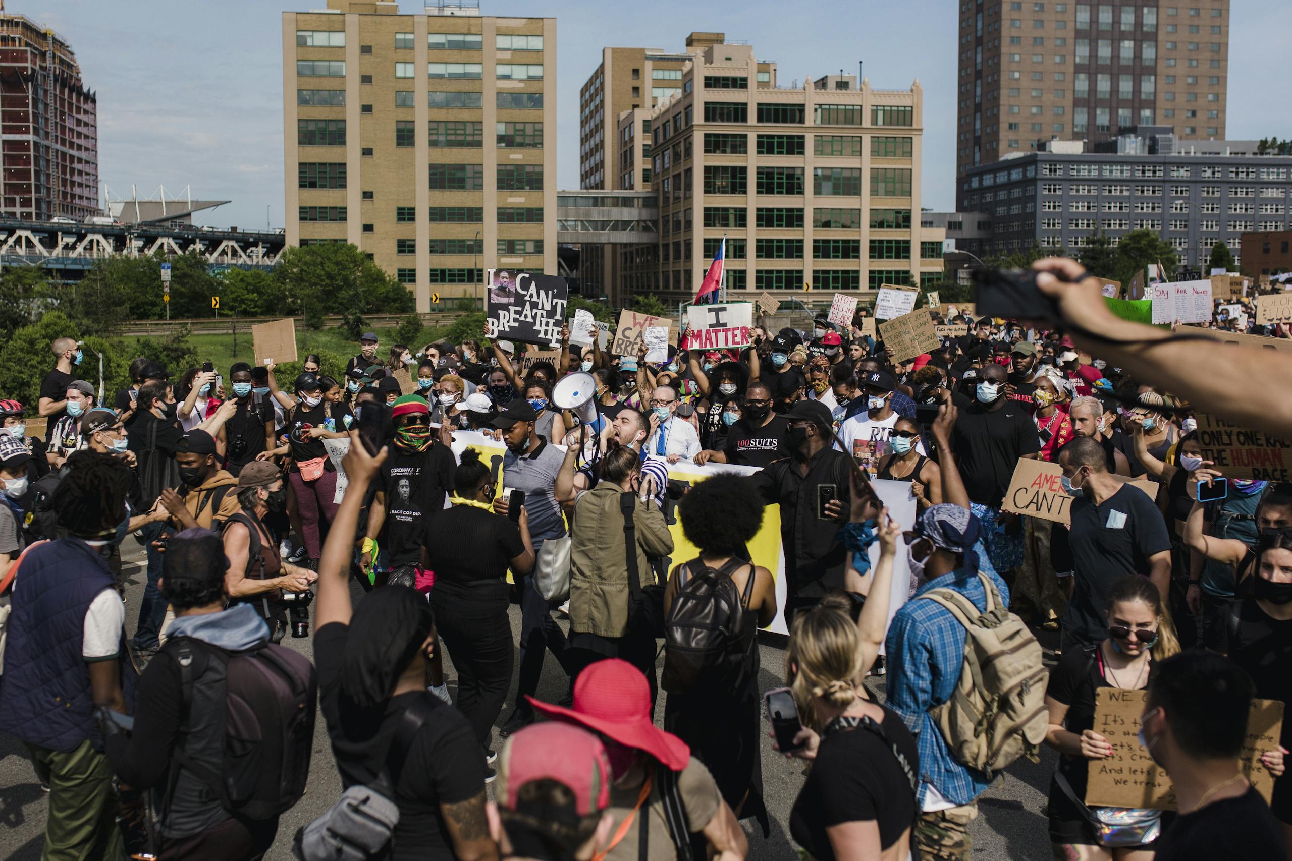 A large and diverse crowd gathers for a peaceful protest advocating for racial justice and equality in an urban setting.