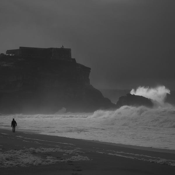 Silhouette on a dark coastal beach with crashing waves and dramatic sky.