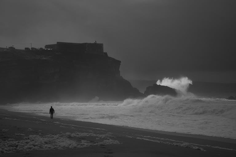 Silhouette on a dark coastal beach with crashing waves and dramatic sky.
