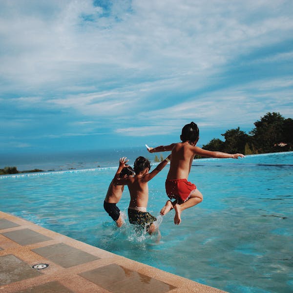 Two children joyfully jump into a pool on a sunny day, embodying excitement and summer vibes.